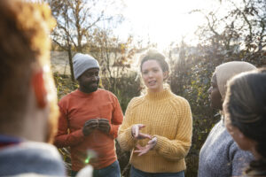 A multiracial group of volunteers wearing warm casual clothing and accessories on a sunny cold winters day. They are talking before they start working on a community farm, planting trees and performing other tasks. | Un groupe multiracial de volontaires portant des vêtements et des accessoires chauds et décontractés lors d'une froide journée d'hiver ensoleillée. Ils discutent avant de commencer à travailler dans une ferme communautaire, à planter des arbres et à effectuer d'autres tâches.