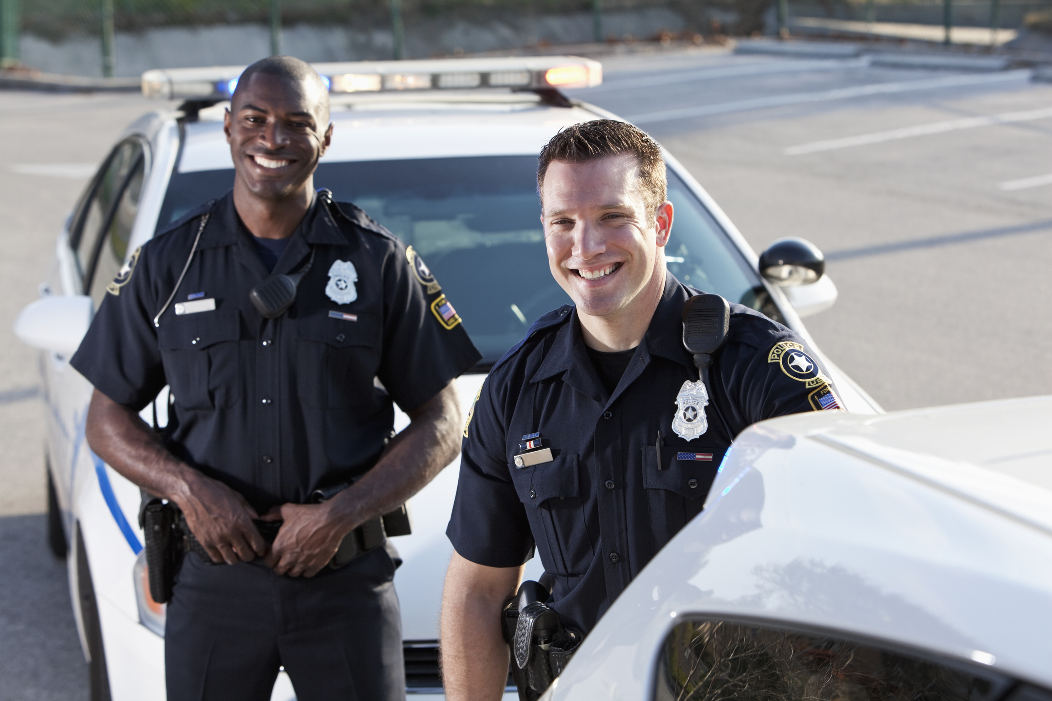 Multi-ethnic police officers (20s) standing in front of police car. | Policiers multiethniques (20 ans) debout devant une voiture de police.