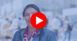 A First Nations woman is smiling in front of a crowd of people. | Une femme des Premières Nations sourit devant une foule de gens.