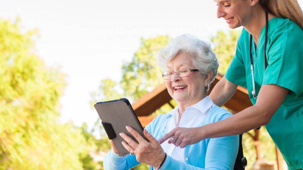 A nurse helping an older woman in a wheelchair with a tablet
