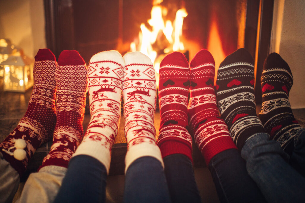 Feet in Christmas socks near fireplace. Four pairs of feet warming up. Friends at cozy winter vacation. | Pieds en chaussettes de Noël près de la cheminée. Quatre paires de pieds en échauffement. Amis en vacances d'hiver douillettes.