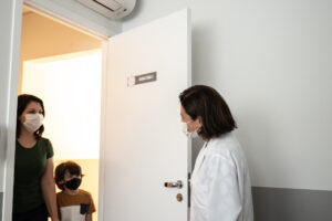 Doctor welcoming patient into her office - wearing protective face mask | Médecin accueillant une patiente dans son bureau - portant un masque de protection