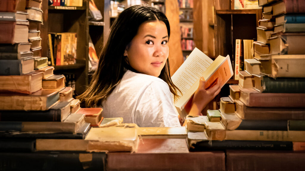 Woman in the library looks back over her shoulder as he reads a book | femme dans la bibliothèque regarde par-dessus son épaule en lisant un livre