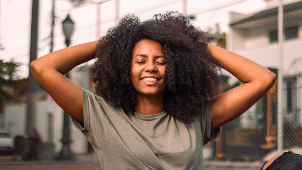 Woman of african-american descent smiles with her eye closed and hands crosed behind her head
