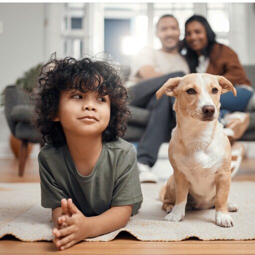 Little boy next to his puppy with the parents sitting on a couch behind him.