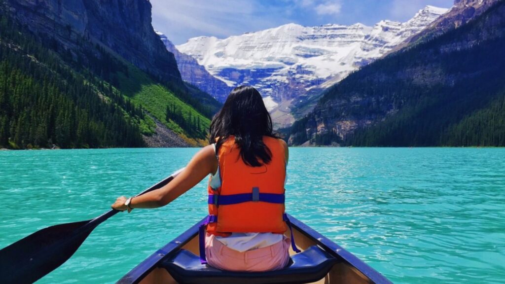 A woman in a life west pedals in canoe across the lake