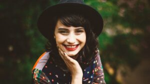 Young woman in a black hat smiles as she looks into the camera