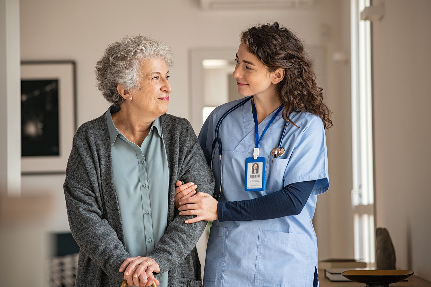 Young caregiver helping senior woman walking. Nurse assisting her old woman patient at nursing home. Senior woman with walking stick being helped by nurse at home. Jeune soignant aidant une femme âgée à marcher. Infirmière aidant sa vieille patiente à la maison de retraite. Senior woman with walking stick étant aidé par une infirmière à la maison.