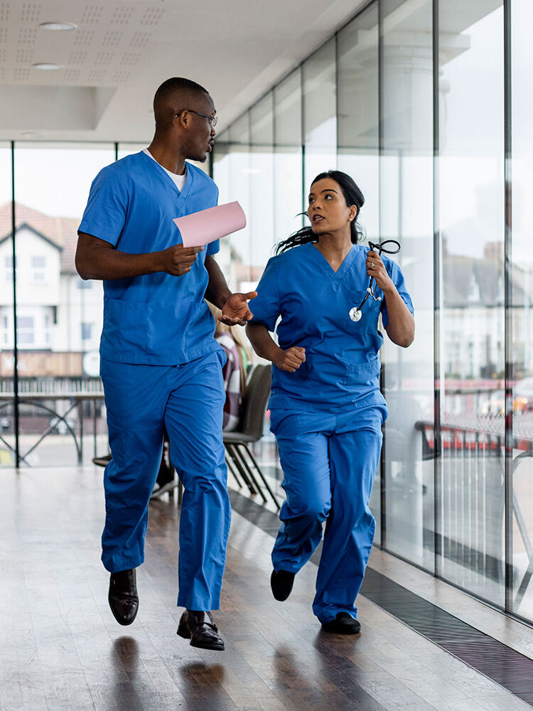 Two health-care workers hurrying down the hallway | Deux travailleurs de la santé au pas de course dans un couloir