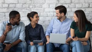 Four young people sitting on a bench against white brick wall talking and laughing