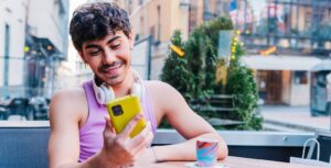 Positive young LGBT person using mobile phone in outdoor cafe