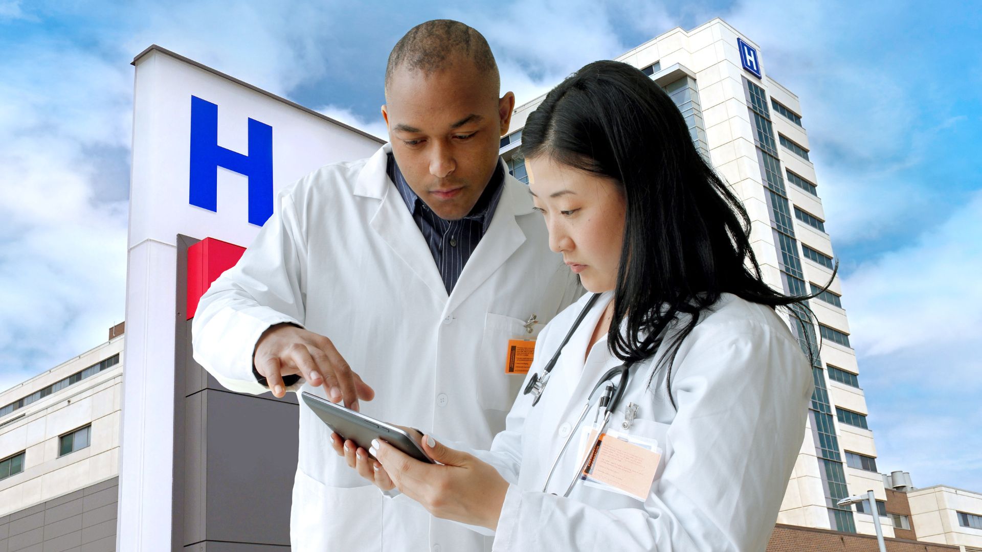 A man and woman in white coats examining a tablet, possibly discussing medical information.
