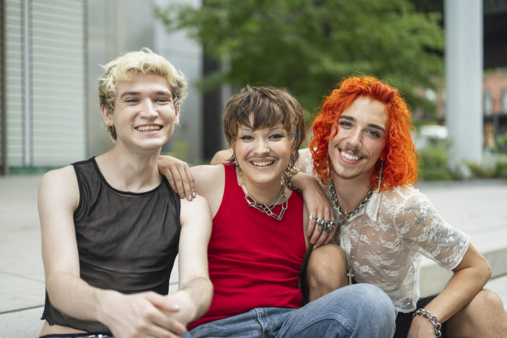 Three friends with colorful hairstyles smiling and posing together outdoors.