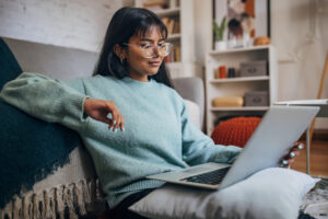 isurely reclined, a woman with stylish glasses uses a laptop in the comfort of her contemporary living area